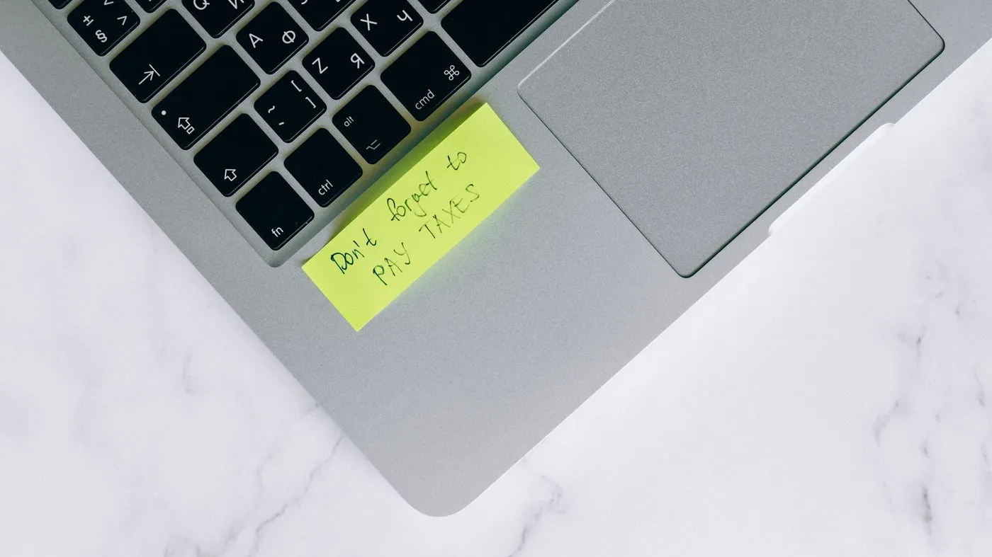 Laptop s poznámkou o placení daní, ilustrace k podnikání s ADHD a papírování
