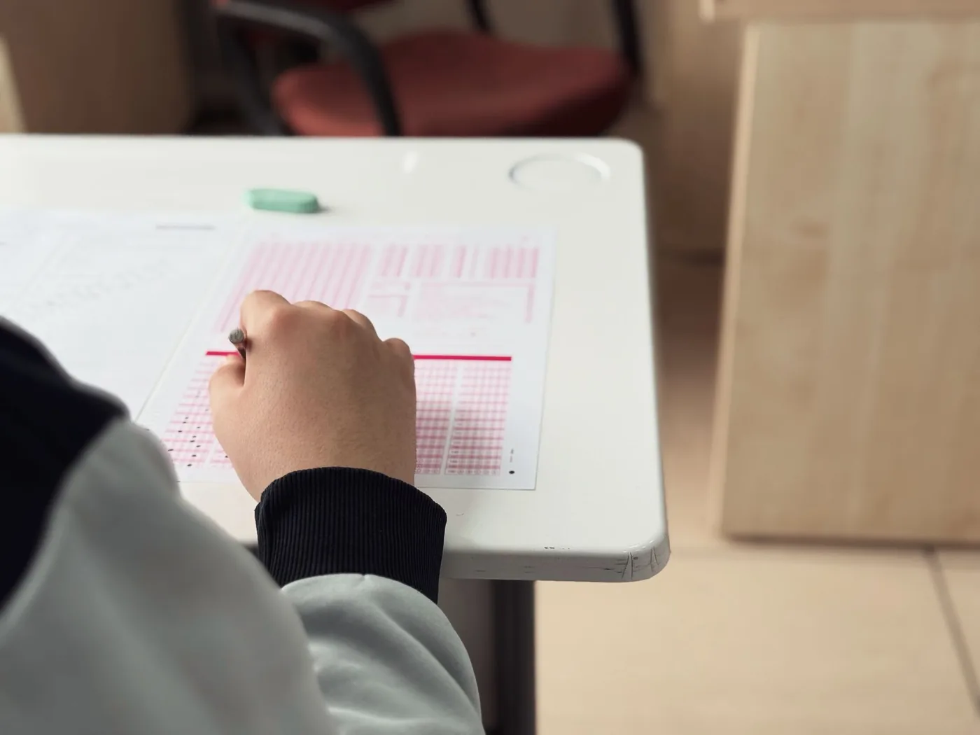 Detail na ruku píšící test s hodinami v pozadí, symbol časového limitu.